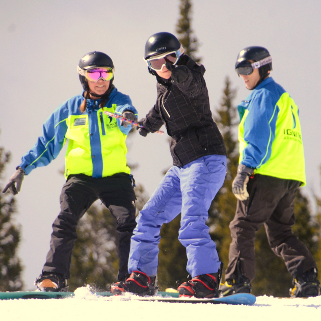 Ignite Athlete snowboarding while being supported by two Ignite Volunteers Instructors