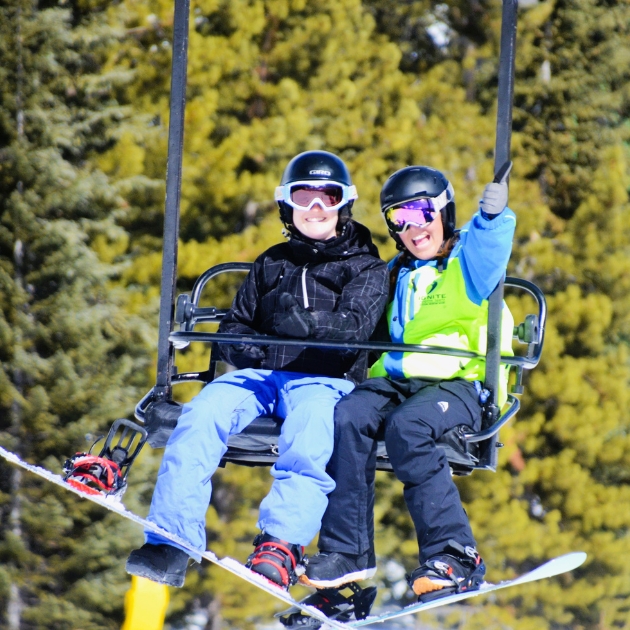 Ignite Athlete and Ignite Volunteer Instructor riding a two-person lift with their snowboards