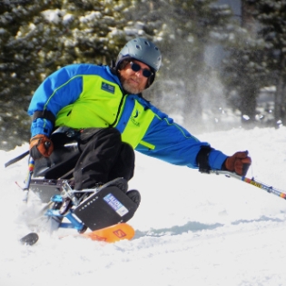 Kevin WIlson riding a sit ski independently in his Ignite Volunteer Instructor jacket