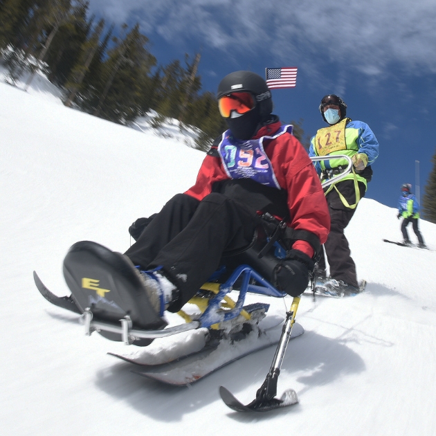 Ignite Veteran Athlete being guided by an Ignite Volunteer Instructor as they go down a run on a sit ski