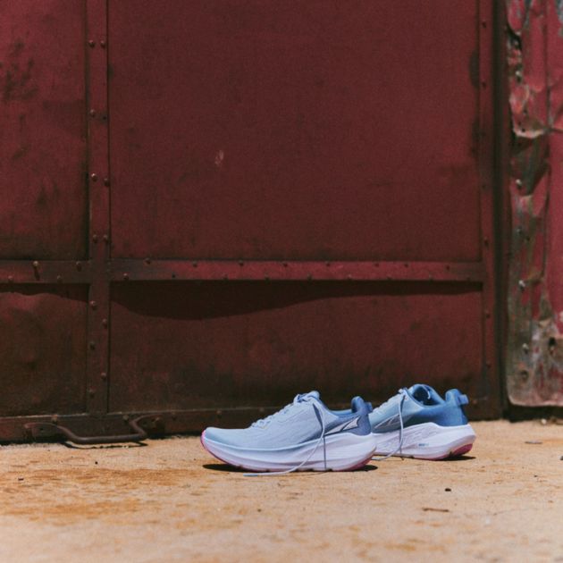 A pair of light blue running shoes resting near a red wall.
