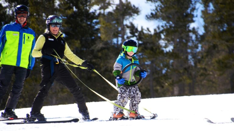 A young Ignite athlete is guided down a snowy slope by two Ignite volunteer instructors during an adaptive skiing lesson.