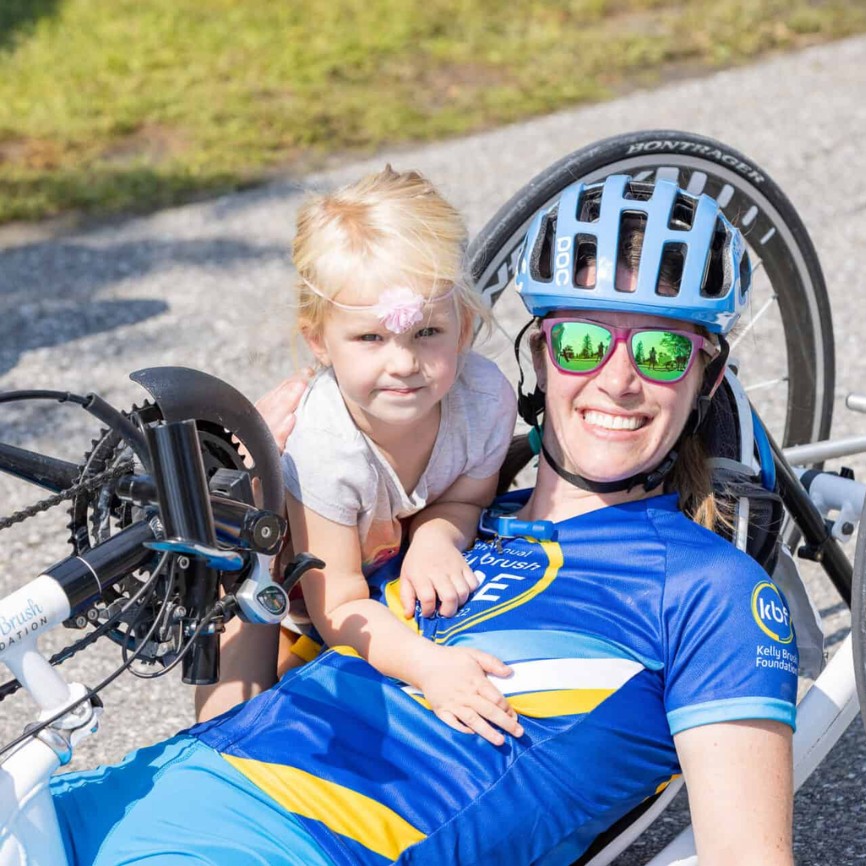 A cyclist with a spinal cord injury shares a happy moment with a young girl while preparing for an adaptive biking event