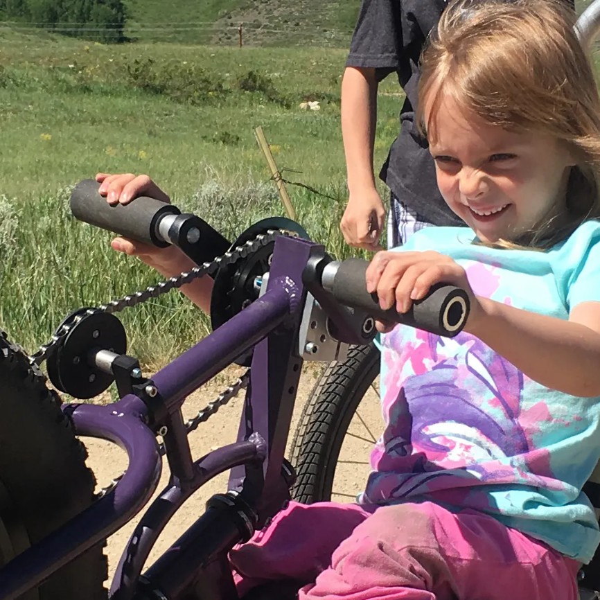 A young girl enthusiastically uses adaptive cycling equipment, enjoying the outdoors with a big smile on her face